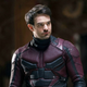 Charlie Cox as Daredevil, wearing the costume, sans mask and looking at a character offscreen.